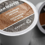 An extreme macro photograph detailing the textured foil lid and embossed KEURIG logo on a coffee K-Cup.