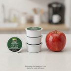 A size comparison image showing a stack of three Green Mountain Half-Caff K-Cup pods next to an apple, with a kitchen appliance in the background.