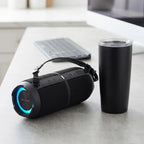 A photorealistic desk scene showing a SHARP GX-BT390 speaker beside a standard black travel tumbler for scale.
