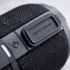 Macro detail of the waterproof connections and fabric mesh on the black GX-BT390 speaker.